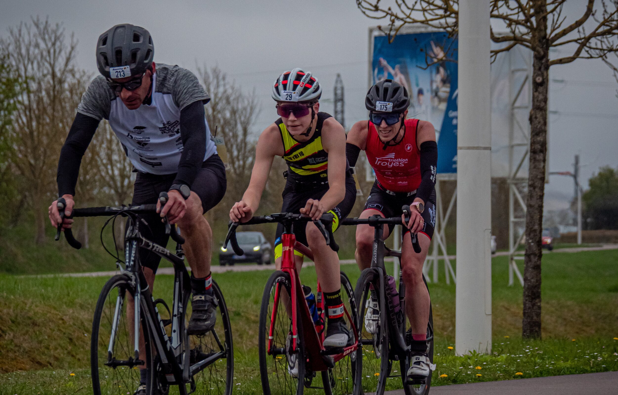 Homme en casquette tenant un trophée doré devant un bâtiment avec pelouse verte.