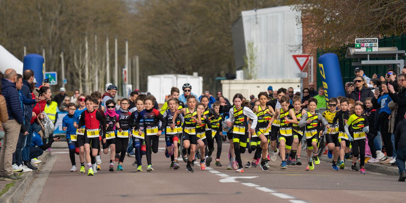 Homme en casquette tenant un trophée doré devant un bâtiment avec pelouse verte.