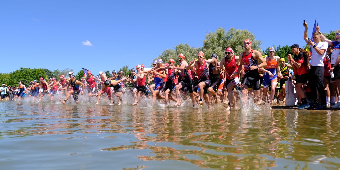 Homme en casquette tenant un trophée doré devant un bâtiment avec pelouse verte.